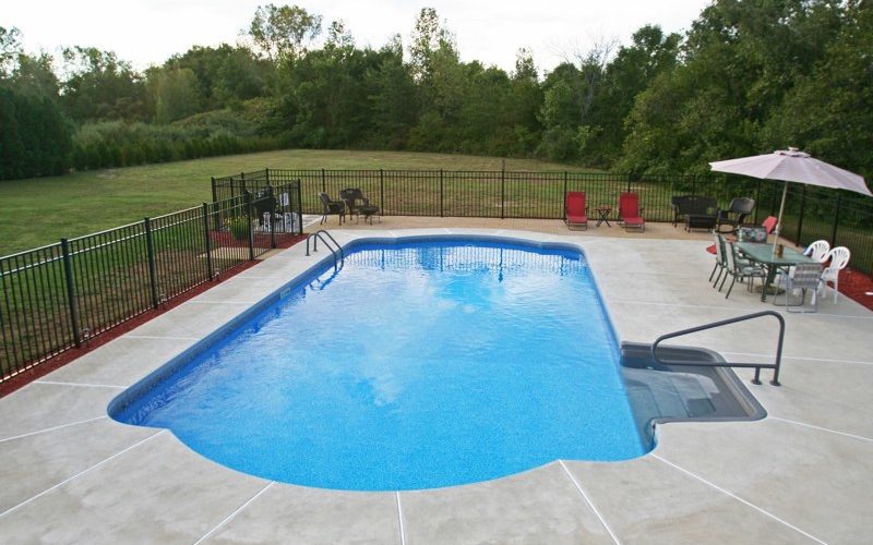 This is a photo of a roman in ground pool in Stuyvesant, NY with custom pavers, black fence and steps.