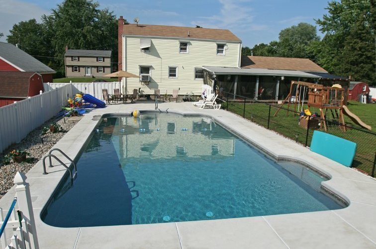 This is a photo of a patrician in ground pool with a house in the background.